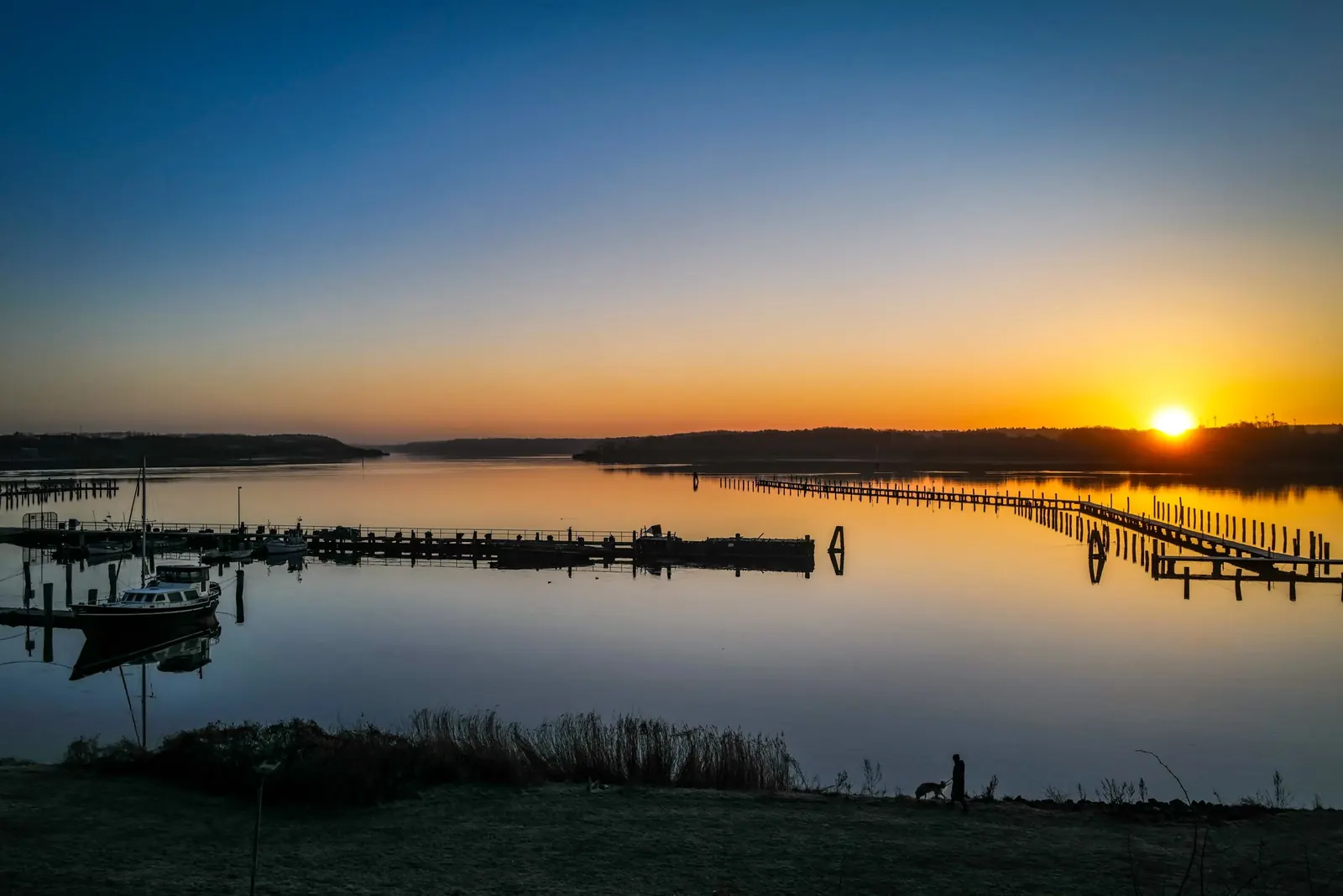 Sonnenaufgang über der Trave bei Lübeck-Schlutup mit Bootsstegen im Vordergrund