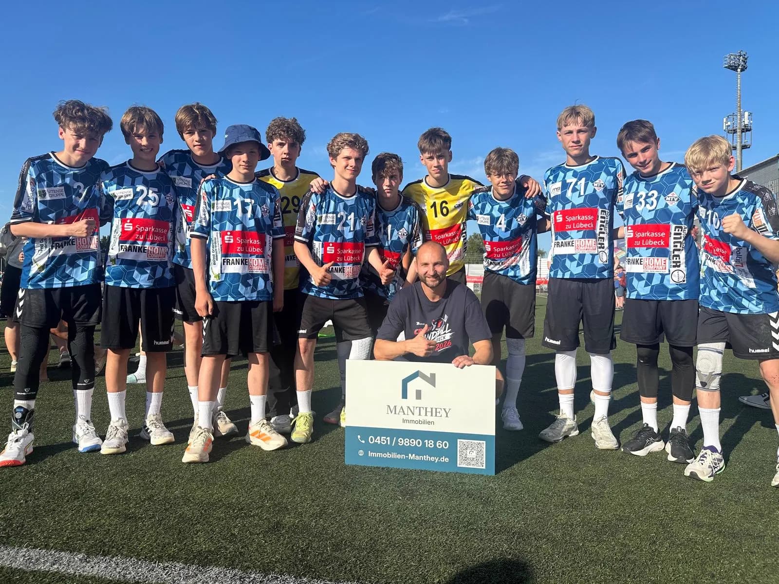 Die C-Junioren-Handballer des MTV Lübeck in Trikots auf dem Kunstrasen, vorne kniet Thomas Manthey mit einem Schild von Manthey Immobilien